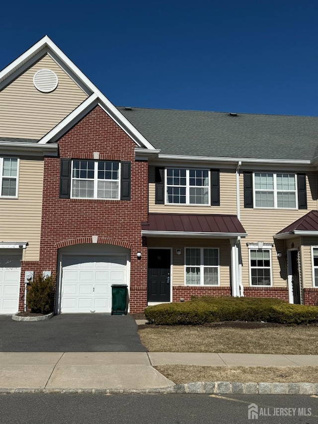 townhome / multi-family property featuring driveway, a standing seam roof, an attached garage, brick siding, and metal roof