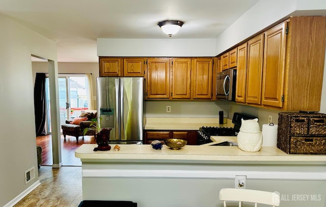 91 Heather Ct, South Brunswick, NJ 08852 - kitchen with stainless steel appliances, a peninsula, brown cabinetry, light countertops, and light wood-type flooring