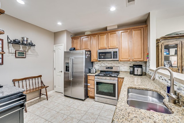kitchen with light stone countertops, a sink, stainless steel appliances, light tile patterned floors, and tasteful backsplash