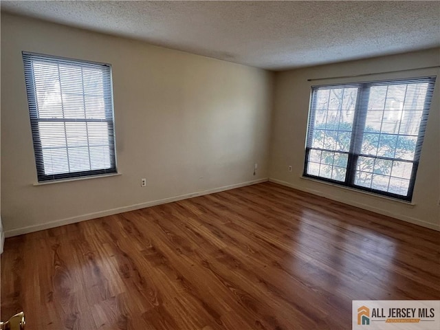 spare room featuring a textured ceiling, baseboards, and wood finished floors