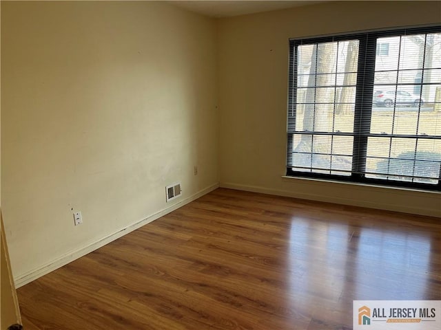 unfurnished room with wood finished floors, visible vents, and baseboards