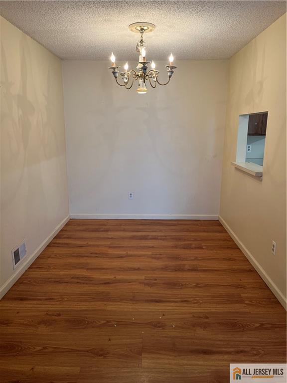 unfurnished room featuring baseboards, visible vents, wood finished floors, an inviting chandelier, and a textured ceiling