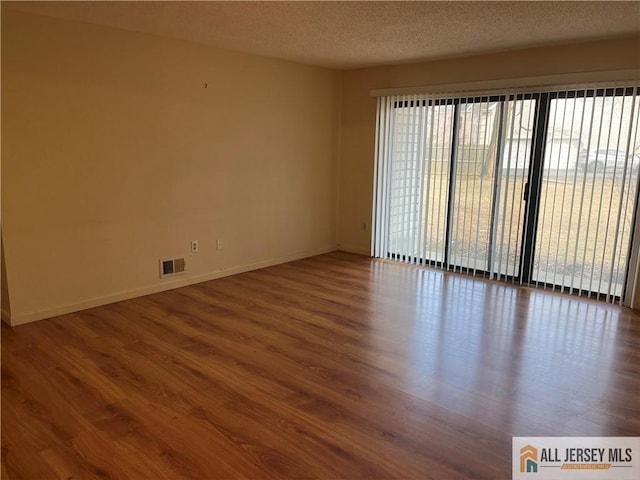 empty room with visible vents, a textured ceiling, baseboards, and wood finished floors