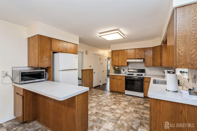 kitchen with gas range oven, freestanding refrigerator, under cabinet range hood, stainless steel microwave, and brown cabinetry