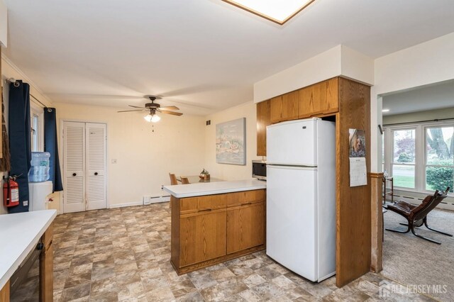 kitchen featuring freestanding refrigerator, a peninsula, brown cabinetry, a ceiling fan, and light countertops