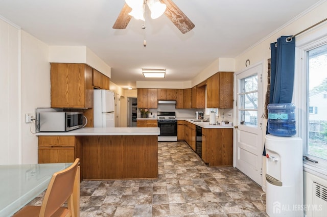 kitchen with stainless steel microwave, range with gas stovetop, freestanding refrigerator, brown cabinetry, and a peninsula