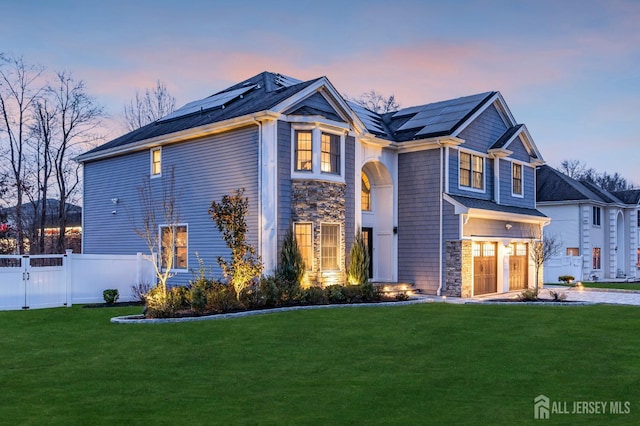 view of front facade featuring solar panels, fence, stone siding, and a lawn