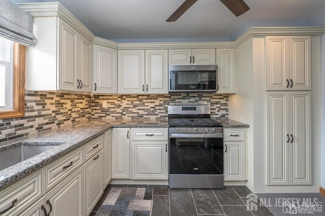 kitchen with stainless steel appliances, ceiling fan, cream cabinetry, and light stone countertops