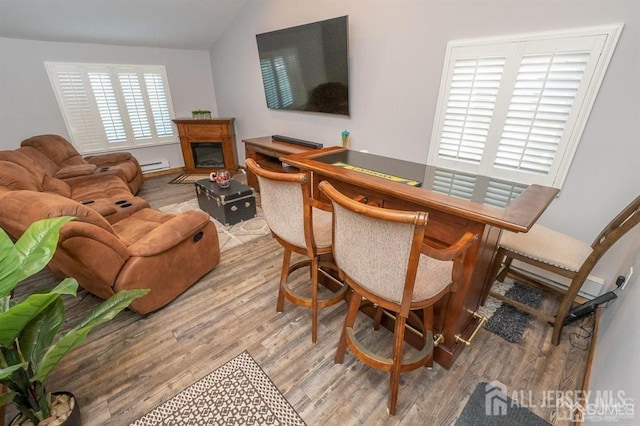 living room with wood finished floors, baseboard heating, a glass covered fireplace, and vaulted ceiling