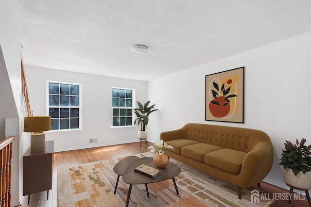 living room with visible vents, a textured ceiling, baseboards, and wood finished floors