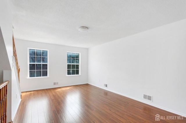 empty room featuring visible vents, baseboards, a textured ceiling, and hardwood / wood-style flooring