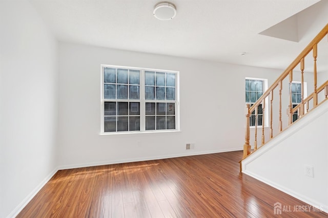 unfurnished room featuring stairway, baseboards, and hardwood / wood-style flooring