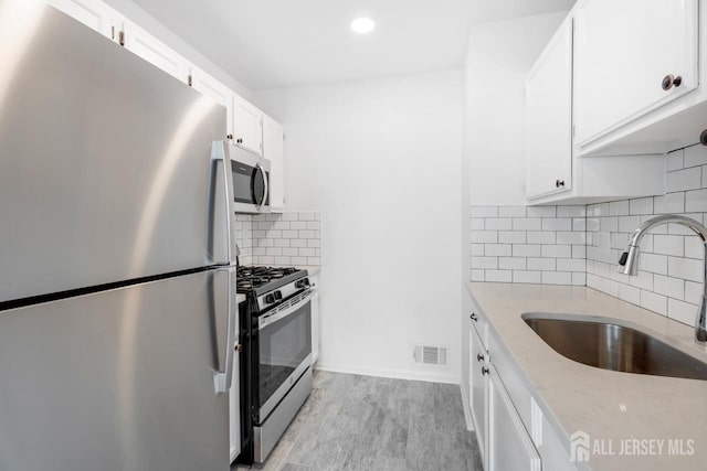 kitchen featuring light stone countertops, visible vents, a sink, stainless steel appliances, and white cabinets