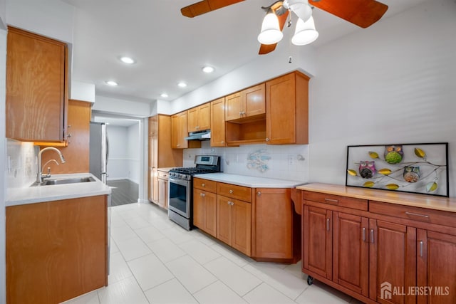 kitchen with light countertops, stainless steel gas stove, under cabinet range hood, and a sink