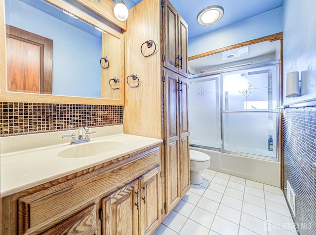 full bathroom featuring vanity, shower / bath combination with glass door, backsplash, tile patterned floors, and toilet