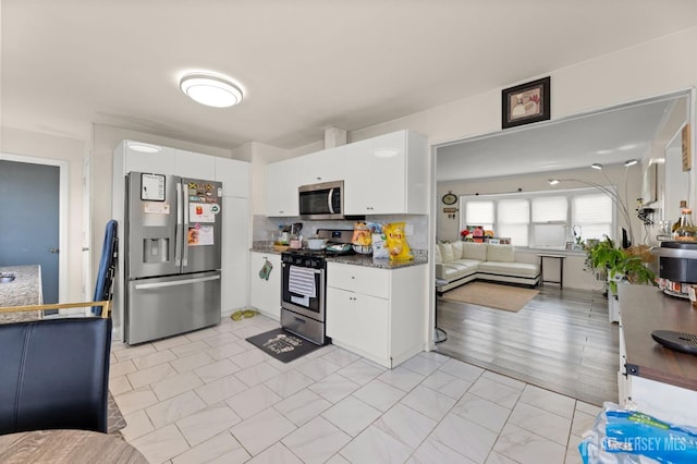 kitchen featuring dark countertops, open floor plan, white cabinetry, stainless steel appliances, and decorative backsplash