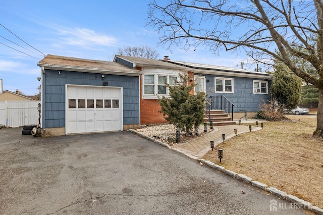 single story home featuring driveway, roof mounted solar panels, an attached garage, and fence