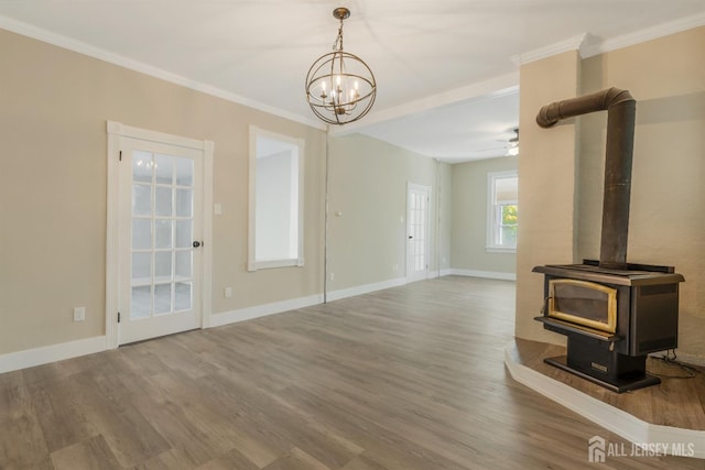 unfurnished living room featuring a wood stove, crown molding, ceiling fan with notable chandelier, and hardwood / wood-style flooring