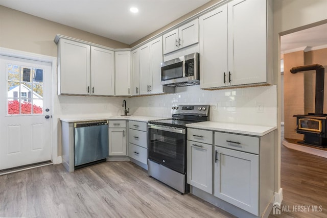 kitchen featuring gray cabinetry, decorative backsplash, a wood stove, and appliances with stainless steel finishes