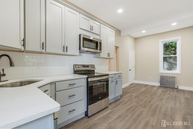 kitchen featuring backsplash, radiator, sink, light hardwood / wood-style flooring, and stainless steel appliances