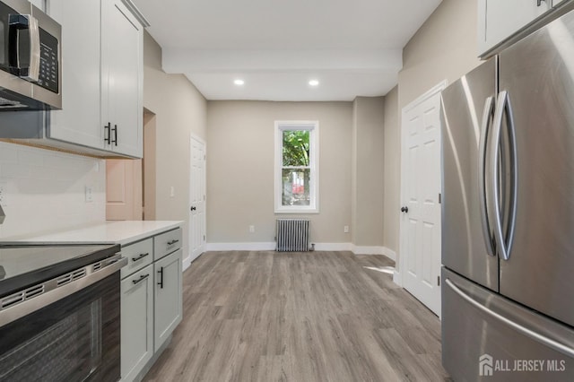 kitchen with tasteful backsplash, radiator, light hardwood / wood-style flooring, and stainless steel appliances