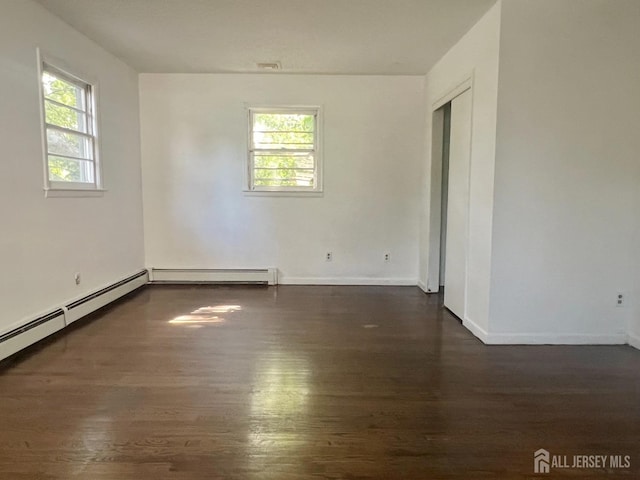 unfurnished room featuring a healthy amount of sunlight, dark hardwood / wood-style floors, and a baseboard heating unit