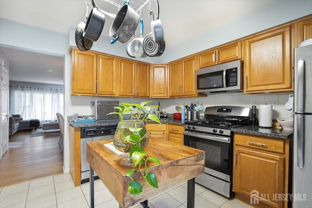 kitchen featuring brown cabinets, light tile patterned flooring, dark countertops, and stainless steel appliances