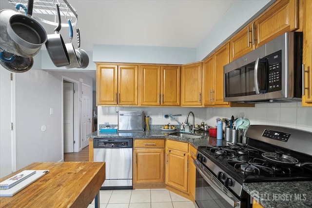kitchen with a sink, appliances with stainless steel finishes, light tile patterned floors, and brown cabinets