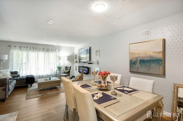 dining area with a textured ceiling, visible vents, wallpapered walls, and wood finished floors