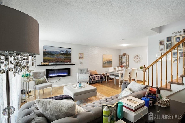 living room featuring a textured ceiling, stairs, a glass covered fireplace, and wood finished floors