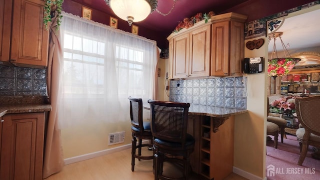 kitchen featuring light wood-type flooring, visible vents, baseboards, and decorative backsplash