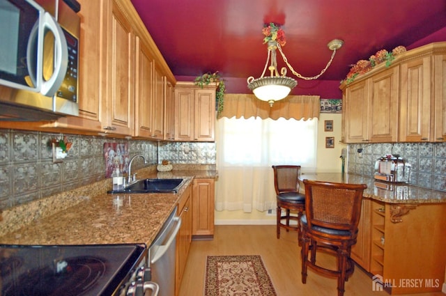 kitchen featuring stainless steel appliances, stone countertops, a sink, light wood-type flooring, and decorative backsplash