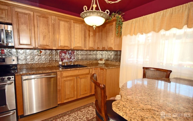 kitchen featuring brown cabinets, stainless steel appliances, a sink, stone counters, and tasteful backsplash