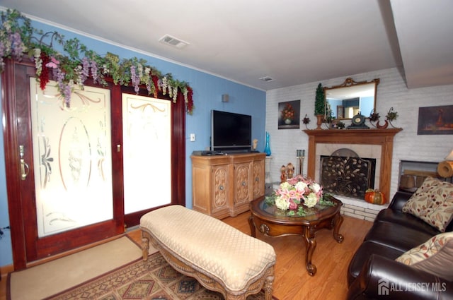 living room with wood finished floors, visible vents, a fireplace with raised hearth, and ornamental molding
