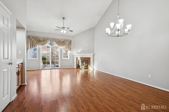 unfurnished living room with ceiling fan with notable chandelier, a tiled fireplace, wood finished floors, and baseboards