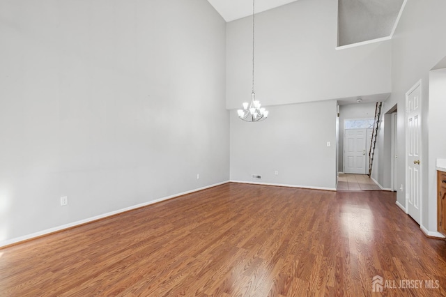 unfurnished room with a notable chandelier, a high ceiling, baseboards, and wood finished floors