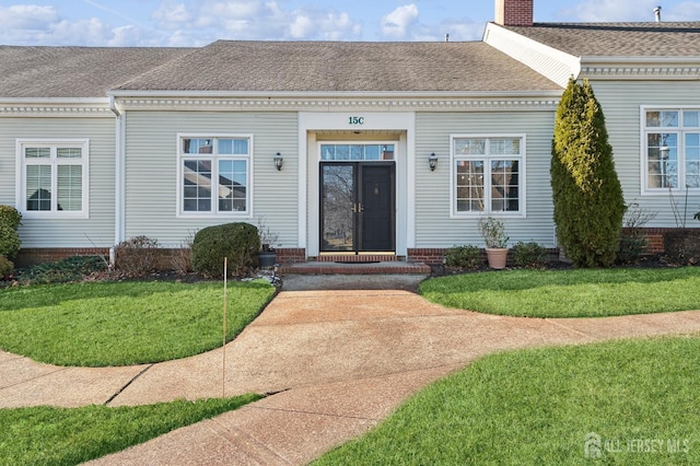 view of exterior entry featuring a chimney, a lawn, and roof with shingles