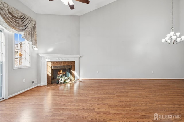 unfurnished living room with visible vents, a tiled fireplace, wood finished floors, baseboards, and ceiling fan with notable chandelier