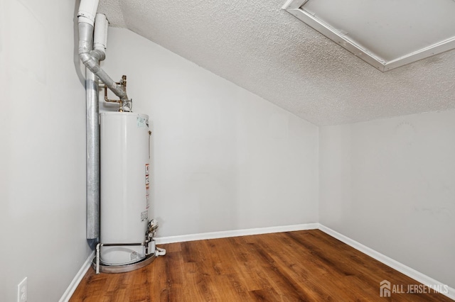 additional living space with gas water heater, vaulted ceiling, a textured ceiling, wood finished floors, and baseboards