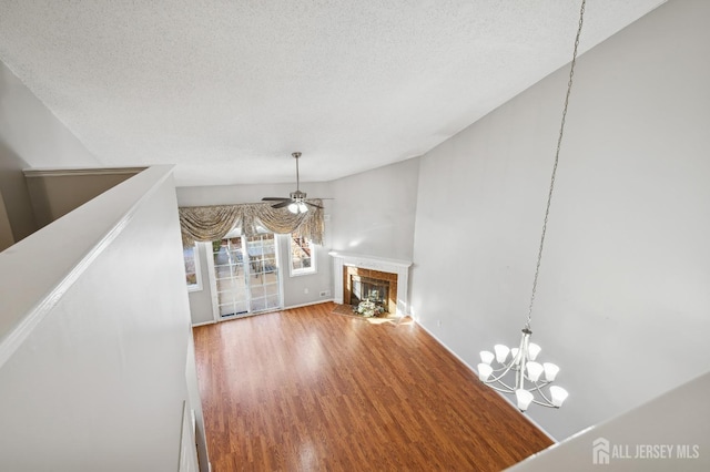 unfurnished living room with a fireplace with flush hearth, ceiling fan with notable chandelier, a textured ceiling, and wood finished floors