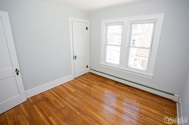 unfurnished room featuring a baseboard heating unit and light hardwood / wood-style floors