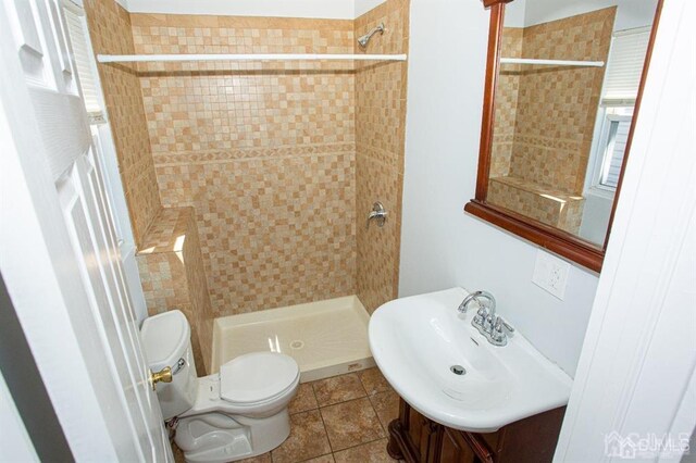 bathroom with toilet, tile patterned floors, sink, and tiled shower