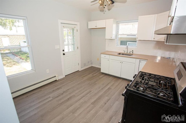 kitchen featuring a baseboard radiator, stainless steel gas range, white cabinetry, sink, and ceiling fan