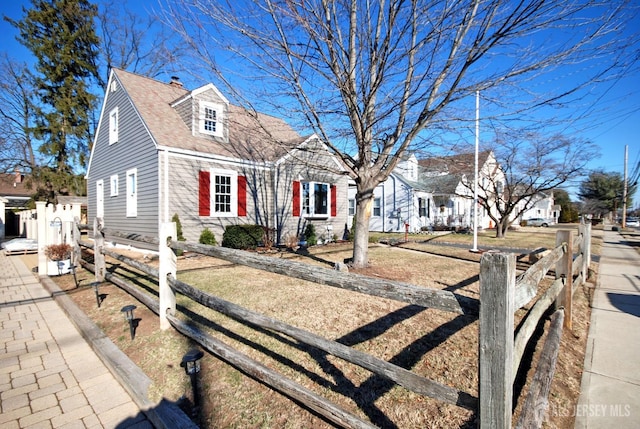 new england style home with a shingled roof, a chimney, and fence