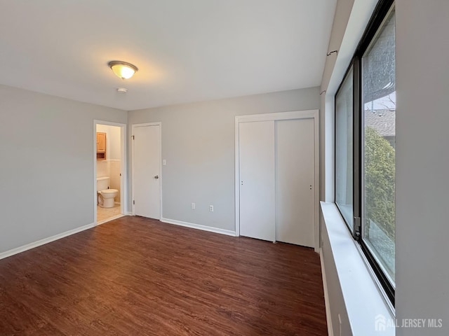 unfurnished bedroom featuring dark wood finished floors, baseboards, and ensuite bathroom