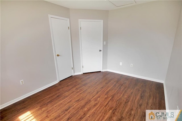 spare room featuring dark wood-style floors, attic access, and baseboards