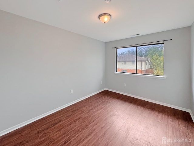 empty room with dark wood-style flooring, visible vents, and baseboards