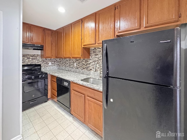 kitchen with a sink, light stone countertops, under cabinet range hood, black appliances, and backsplash