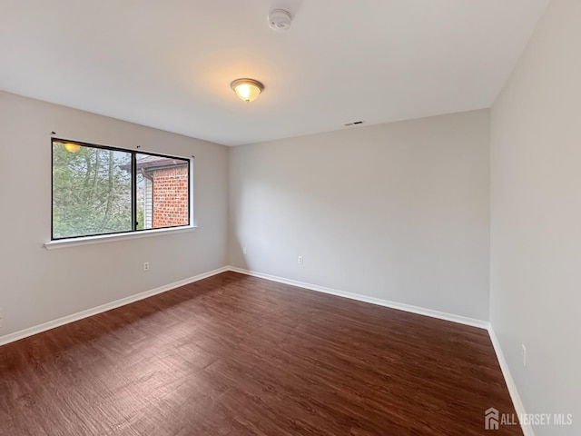 empty room with dark wood-style flooring, visible vents, and baseboards