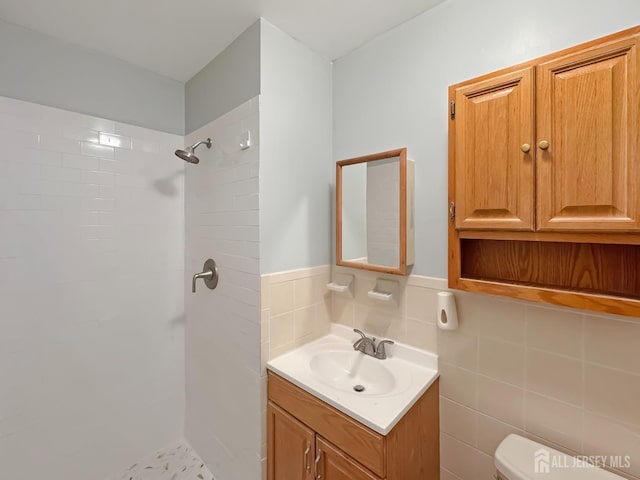 full bathroom with toilet, a wainscoted wall, vanity, tile walls, and tiled shower